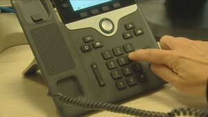 Osoba wybiera palcem numer na klawiaturze telefonu stacjonarnego.