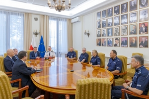 Uczestnicy uroczystości podpisania porozumienia siedzą przy stole w kształcie elipsy.
