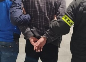 Zatrzymany mężczyzna zakuty w kajdanki trzymany przez dwóch policjantów.