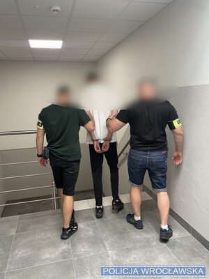 Dwaj policjanci prowadzą zatrzymanego w kajdankach.