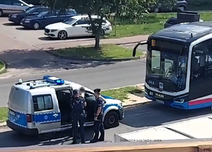 Policjanci stoją przy radiowozie, obok autobus miejski.