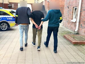 Dwaj funkcjonariusze prowadzą chodnikiem zatrzymanego mężczyznę zakutego w kajdanki.