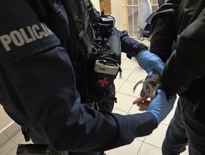 Policjant zakłada kajdanki zatrzymanemu mężczyźnie.