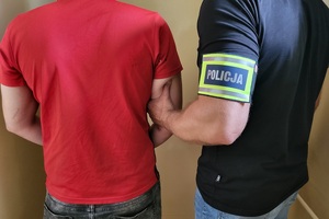 Policjant trzyma zatrzymanego w kajdankach.