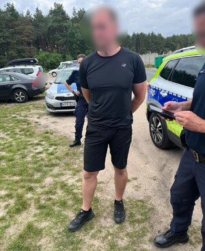 Stojący mężczyzna, a wokół niego widać policjantów i radiowozy.