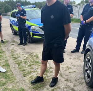 Stojący mężczyzna, a wokół niego widać policjantów i radiowozy.