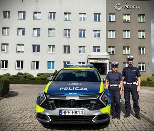 Policjanci stoją obok radiowozu.