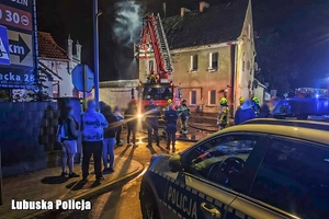 Policjanci i strażacy podczas akcji przy płonącym budynku.