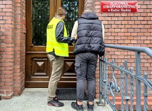 Funkcjonariusz z zatrzymaną osobą w kajdankach.