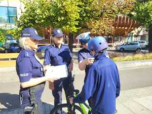 Dwie policjantki stoją obok policjanta, który zakłada kask chłopcu.