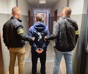 Dwóch policjantów z zatrzymanym mężczyzną zakutym w kajdanki.
