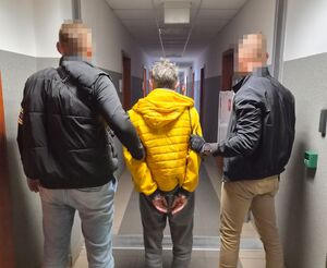 Dwóch policjantów z zatrzymanym mężczyzną zakutym w kajdanki.