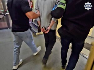 Zatrzymanego mężczyznę w kajdankach prowadzą korytarzem nieumundurowani policjanci.