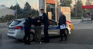 tacja benzynowa, policjanci prowadzą do radiowozu zatrzymanego.