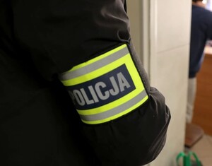 Zbliżenie na opaskę z napisem Policja, która znajduje się na ramieniu.