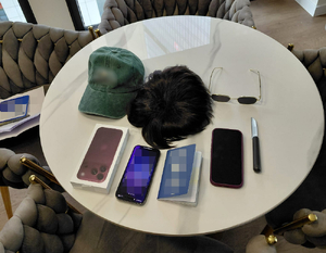 Na stole leżą: peruka, czapaka z daszkiem, okulary słoneczne, telefon komórkowy, notes.