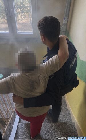 Policjant pomaga starszej kobiecie wyjść z budynku.
