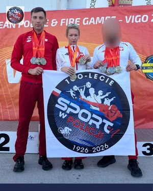 Dwaj zawodnicy i zawodniczka z medalami zawieszonymi na szyjach. Wspólnie trzymają banner z logiem 100-lecia sportu w Policji.