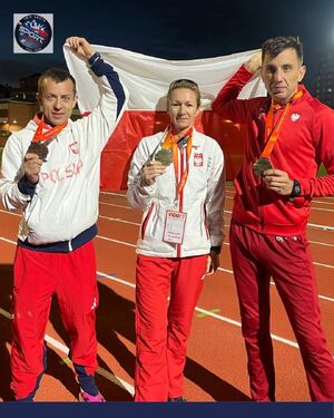 Dwaj zawodnicy i zawodniczka z medalami na szyjach. W górze trzymają polską flagę.