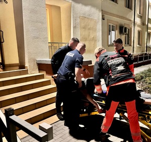 Dwaj policjanci i dwaj ratownicy medyczni przy noszach, na których lezy mężczyzna.
