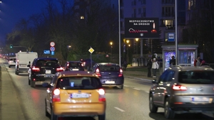 Zmrok. Samochody jadące ulicą. Trzy osoby stojące na przystanku.
