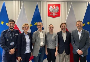 Sześć osób, uczestników i uczestniczek spotkania w Komendzie Głównej Policji. Na zdjęciu są przedstawiciele Policji oraz Biura Instytucji Demokratycznych i Praw Człowieka stojący na tle flag Polski i Unii Europejskiej.