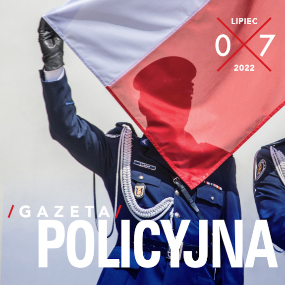 Policjant trzyma za róg polską flagę która zasłania jego twarz.