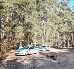 policyjne radiowozy zaparkowane w terenie leśnym, w miejscu startu policyjnego drona
