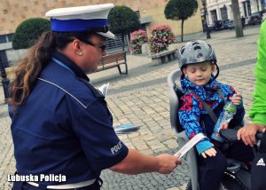 Policjantka nakłada element odblaskowy dziecku na rowerze.