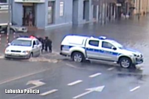 policjanci pchają samochód na zalanej ulicy