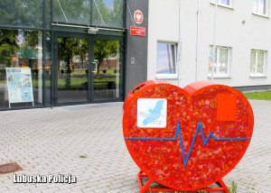 Metalowy, czerwony pojemnik w kształcie serca, przed  komendą Policji.