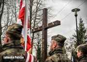 Stojący w szeregu żołnierze, a w tle krzyż - Pomnik Ofiar Katynia.