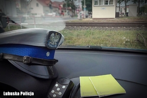 Zdjęcie z wnętrza radiowozu z czapką policjanta drogówki na pulpicie na tle torowiska