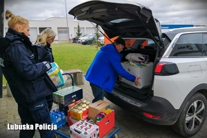 Policjanci pakują zebrane przedmioty oraz żywność do bagażnika pojazdu