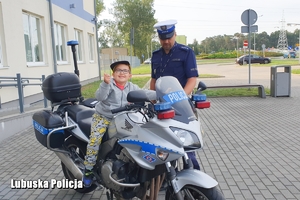 Mały chłopiec siedzący na policyjnym motocyklu w towarzystwie policjanta.
