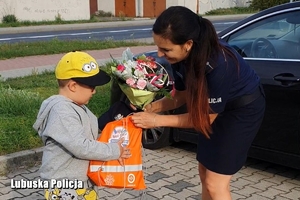 Chłopiec wręcza kwiaty policjantce, a policjantka chłopcu torbę z prezentami.