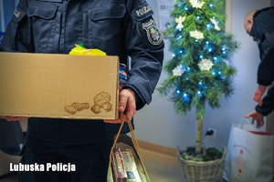 Policjant przenosi prezenty, w tle choinka.