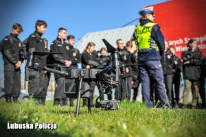 dron stojący na trawniku a w tle policjantka rozmawia z uczniami klasy mundurowej