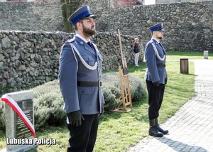 Policjanci pełnia posterunek honorowy przed pomnikiem.