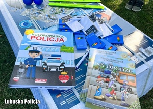 Policyjne kolorowanki, kredki oraz elementy odblaskowej umieszczone na kartonie.