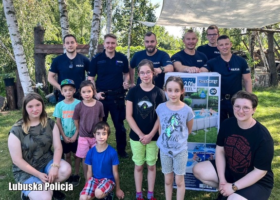 Policjanci oraz dzieci pozują do zdjęcia w ogrodzie.