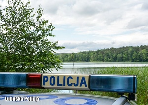 Policyjny radiowóz, a w tle jezioro.