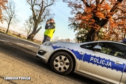 Policjant drogówki stojący przy radiowozie podczas kontroli prędkości jadących pojazdów.