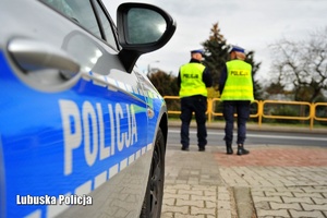 Radiowóz policyjny, a w tle policjanci ruchu drogowego.