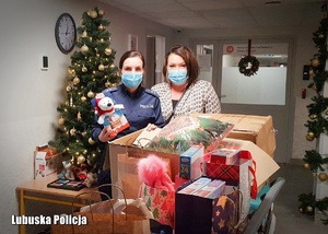 Policjantka oraz kobieta stoją przy kartonach pełnych prezentów świątecznych.