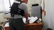 Policjant w kamizelce pokazuje rozłożone na biurku nielegalne przesyłki