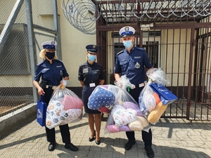 Policjanci i pracownik służby więziennej trzymają torby z maskotkami