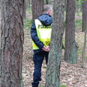 Policjant stoi tyłem między drzewami