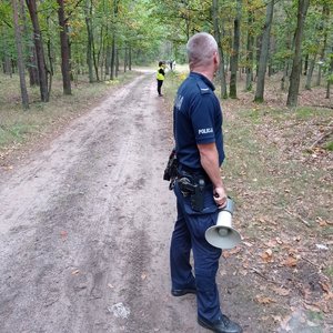 Policjant stoi z tubą w lesie za nim stoi kilkoro innych