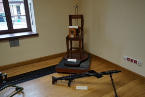 eksponaty w sali muzeum: broń oraz krzesło sygnalityczne z podstawą i aparatem analogowym